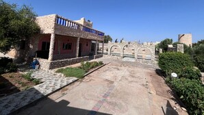 Un edificio in pietra con un balcone, un cortile lastricato e un muro in pietra con archi.