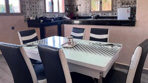 Zona pranzo con tavolo e sedie, cucina con frigorifero e piastrelle decorate alle pareti.