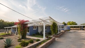 Una casa con porche cubierto, jardín con diversas plantas y cielo despejado.