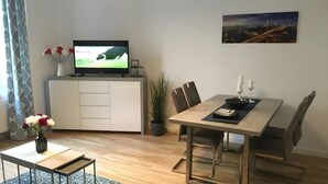 A modern living room with a flat-screen TV, a dining table with chairs, a vase with flowers, and a potted plant. - Apartment for 4 Guests, 55 m², with Wi-Fi (Berlin)