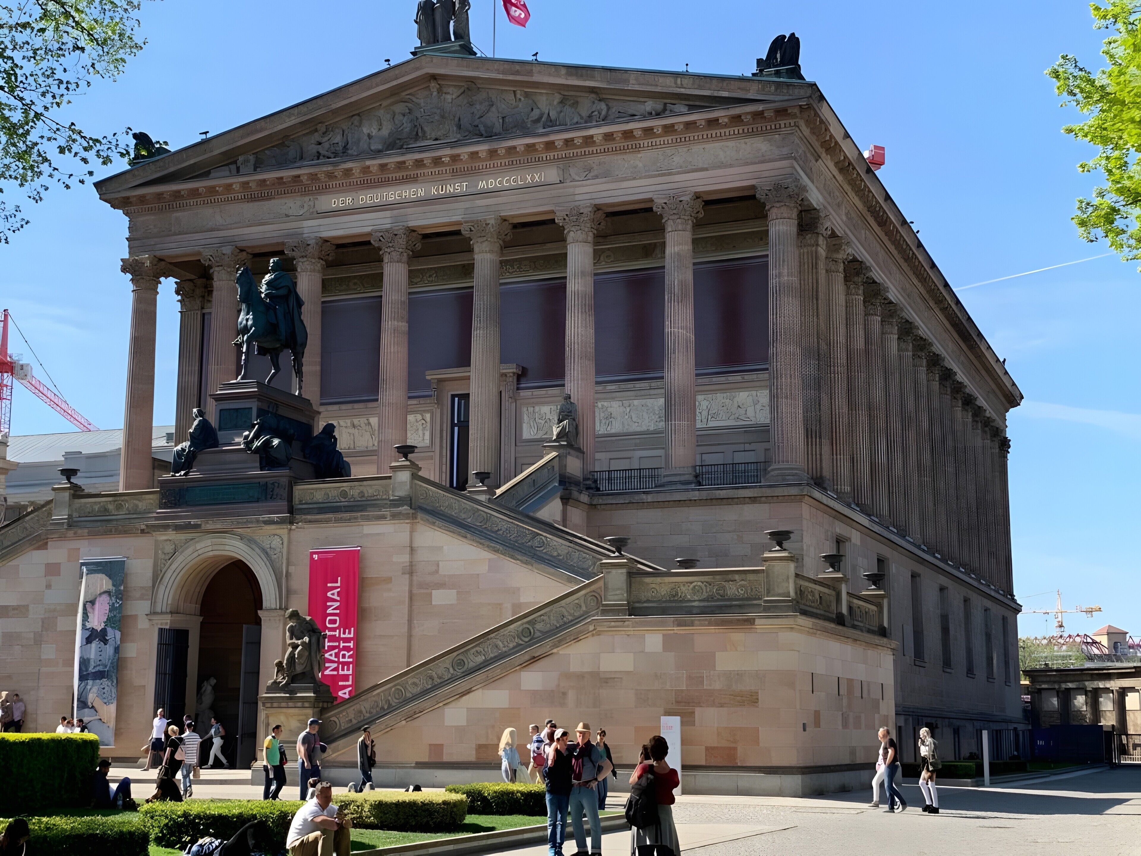 A classical building with a central statue, a flag, and a staircase leading to an entrance.