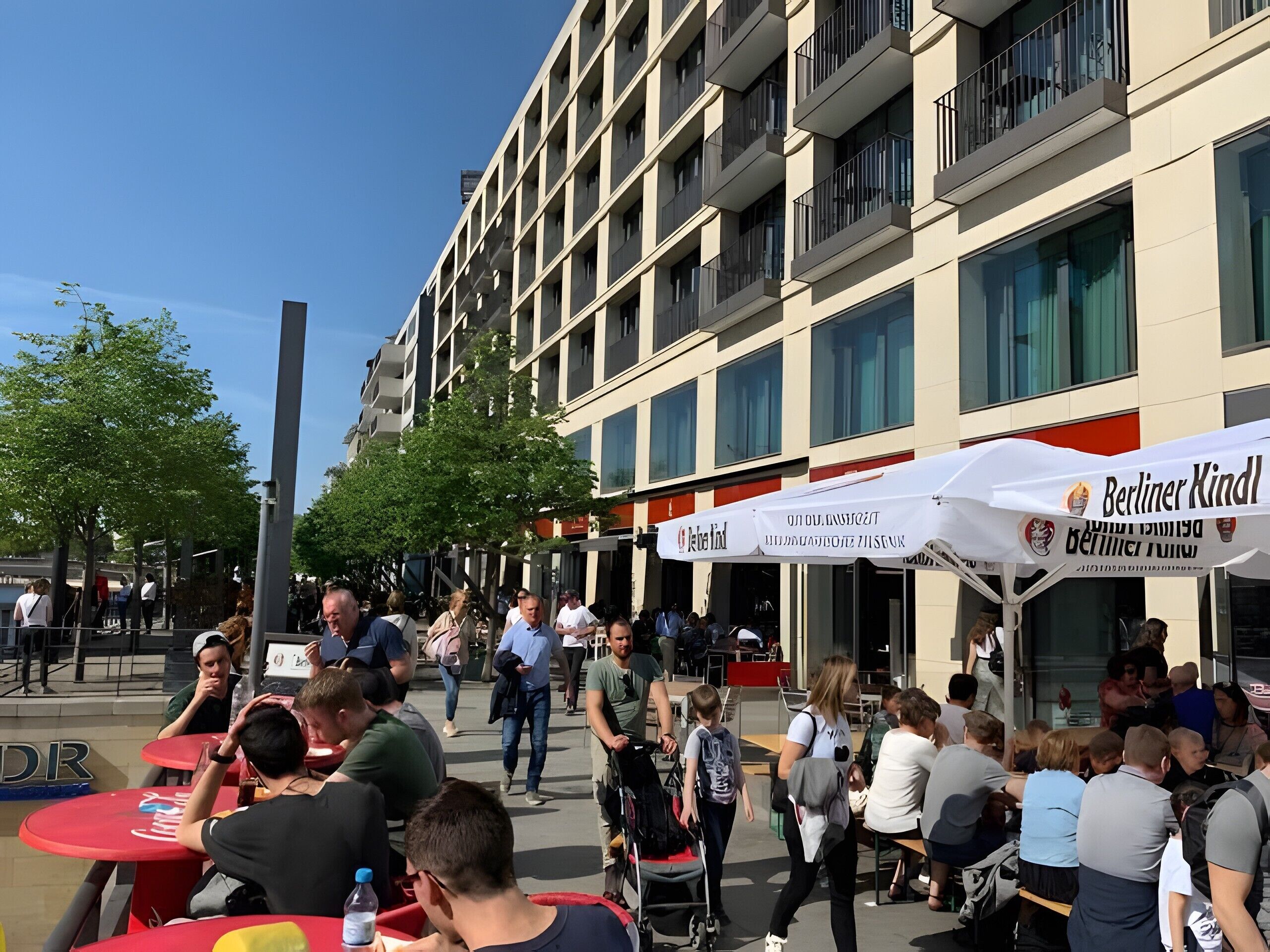 An outdoor seating area with tables and chairs, a building with balconies, and a clear sky.