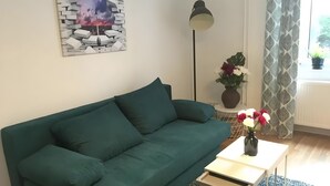 A living room with a green sofa, a small table, a floor lamp, a wall art piece, and a window with curtains. - Apartment for 4 Guests, 55 m², with Wi-Fi (Berlin)