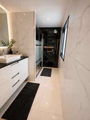 Un baño moderno con un espejo grande, un lavamanos blanco y una zona de ducha.