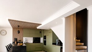 A modern kitchen with green cabinets, a marble island, and a staircase leading to an upper level. - Sunny Algarve: Duplex with ocean views in Armação de Pêra. (Armação de Pêra)
