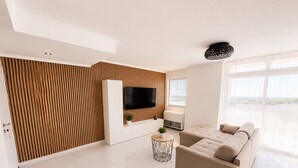 A modern living room with a flat-screen TV, a sofa, a small round table, and a potted plant. - Sunny Algarve: Duplex with ocean views in Armação de Pêra. (Armação de Pêra)
