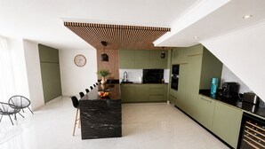 A modern kitchen with a central island, green cabinetry, and a dining area with a black marble table. - Sunny Algarve: Duplex with ocean views in Armação de Pêra. (Armação de Pêra)