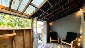 En overdækket veranda med en træbænk, en dør der fører ud, og en tæppe med et mønster.