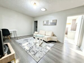 A modern living room with a sofa, a glass coffee table, a black chair, and a wooden TV stand. - Modern Cottage Near Beaches Subway Free Private Parking (Toronto)