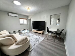 A modern living room with a sofa, TV, and dining area. - Modern Cottage Near Beaches Subway Free Private Parking (Toronto)