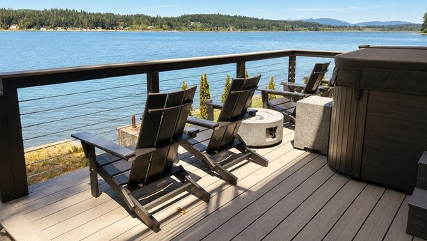 Een terras met buitenmeubilair, een jacuzzi en uitzicht op een meer.