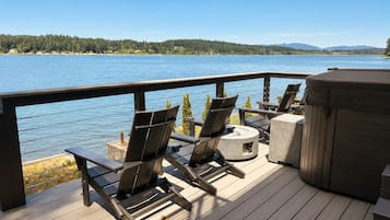Une terrasse avec coin salon extérieur, un jacuzzi et une vue sur un lac.