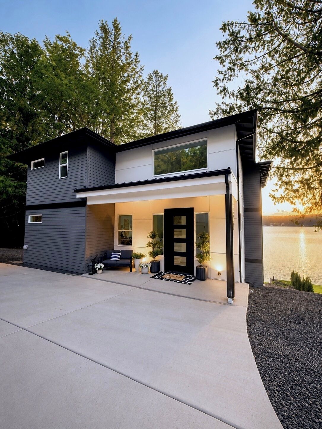 Une maison moderne à deux étages, dotée d’un garage fermé, d’un porche à l’avant avec des sièges et offrant une vue sur un lac.
