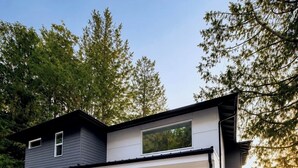 Een modern huis met twee verdiepingen, een overdekte garage, een veranda met zitplaatsen en uitzicht op een meer.