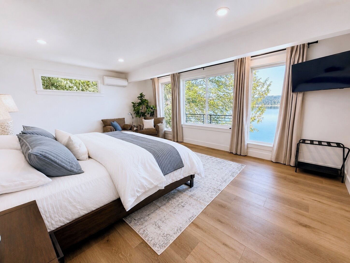 Une chambre moderne avec un grand lit, une télévision, une fenêtre donnant sur un lac et une plante.
