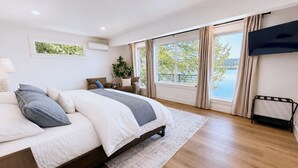Een moderne slaapkamer met een groot bed, een televisie, een raam met uitzicht op een meer en een plant.