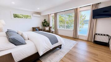 Une chambre moderne avec un grand lit, une télévision, une fenêtre donnant sur un lac et une plante.