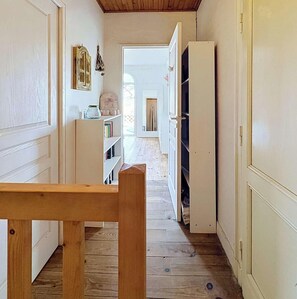 Ein schmaler Korridor mit Holzdielen, weißen Wänden und einer Holzbank.