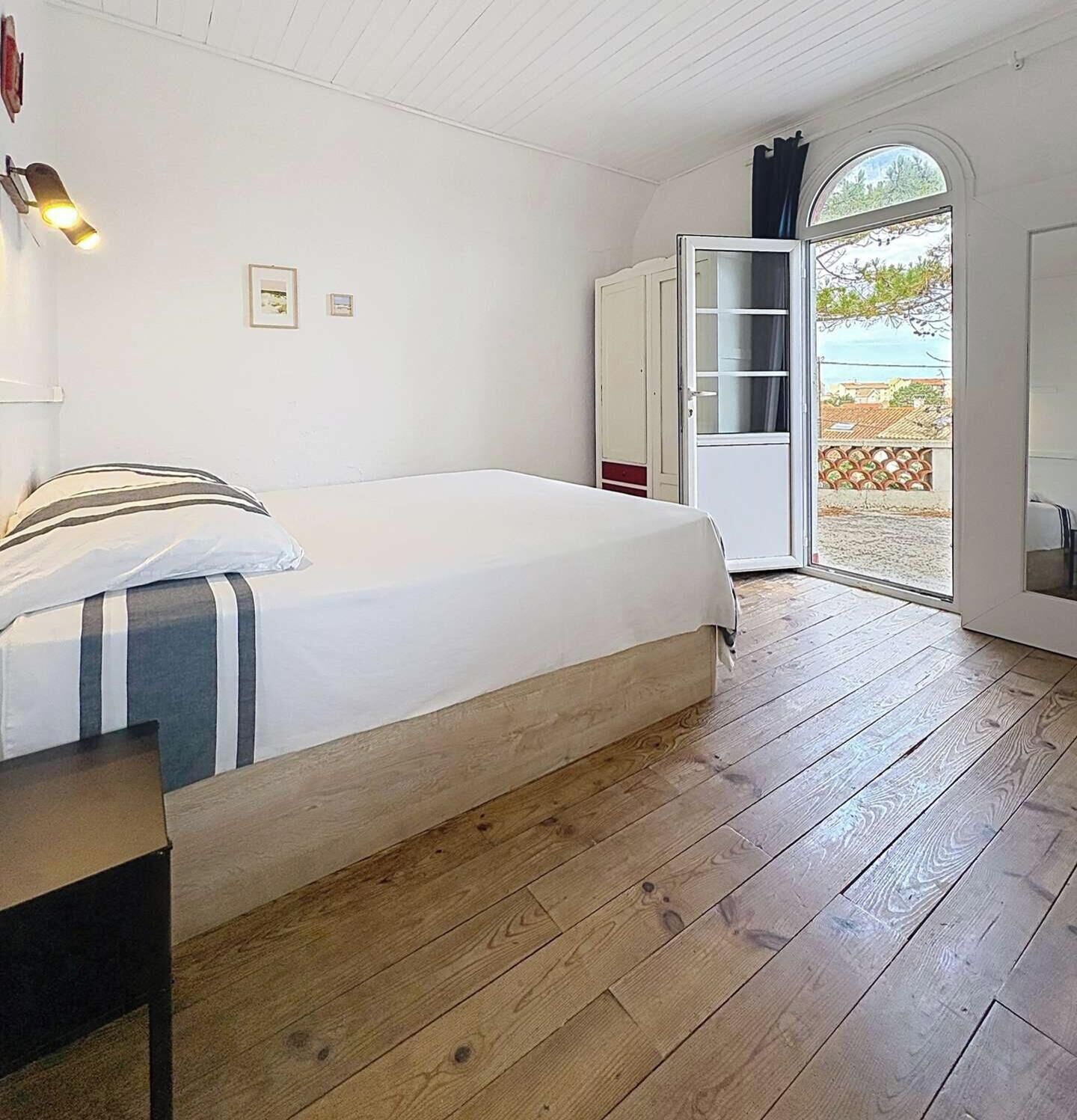 Een slaapkamer met een bed, houten vloeren, een kledingkast en een deur naar een buitenruimte.