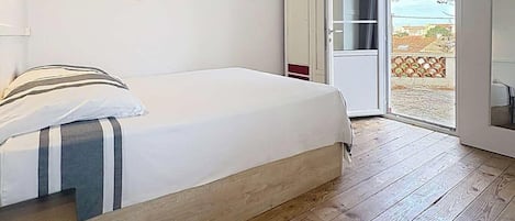 Une chambre à coucher comprenant un lit, un plancher en bois, une armoire et une porte donnant sur un espace extérieur.