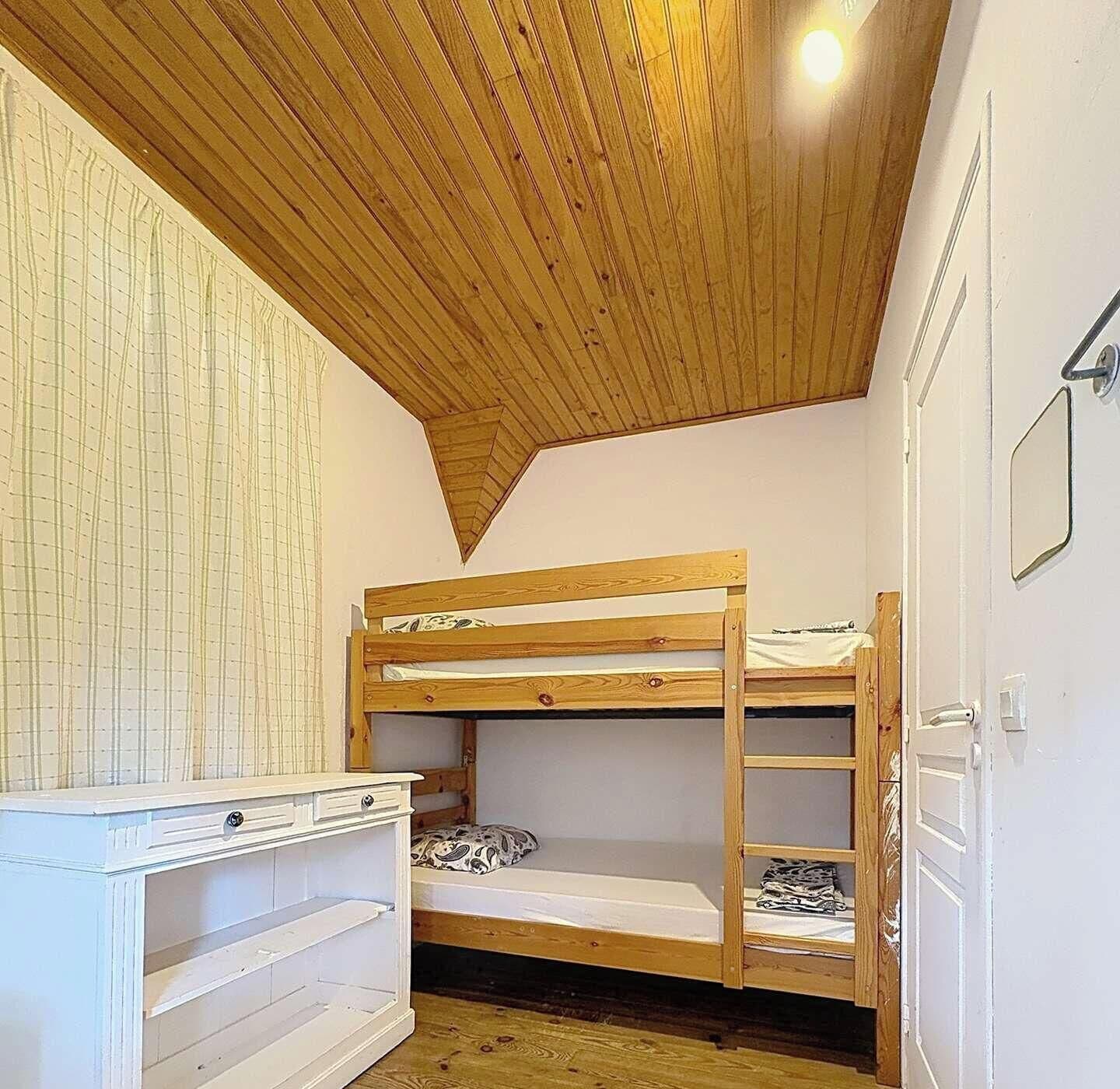 A bunk bed room with a sloped ceiling and a white dresser.