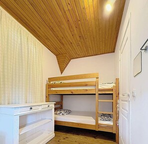 Une chambre avec un lit superposé, un plafond en pente et une commode blanche.