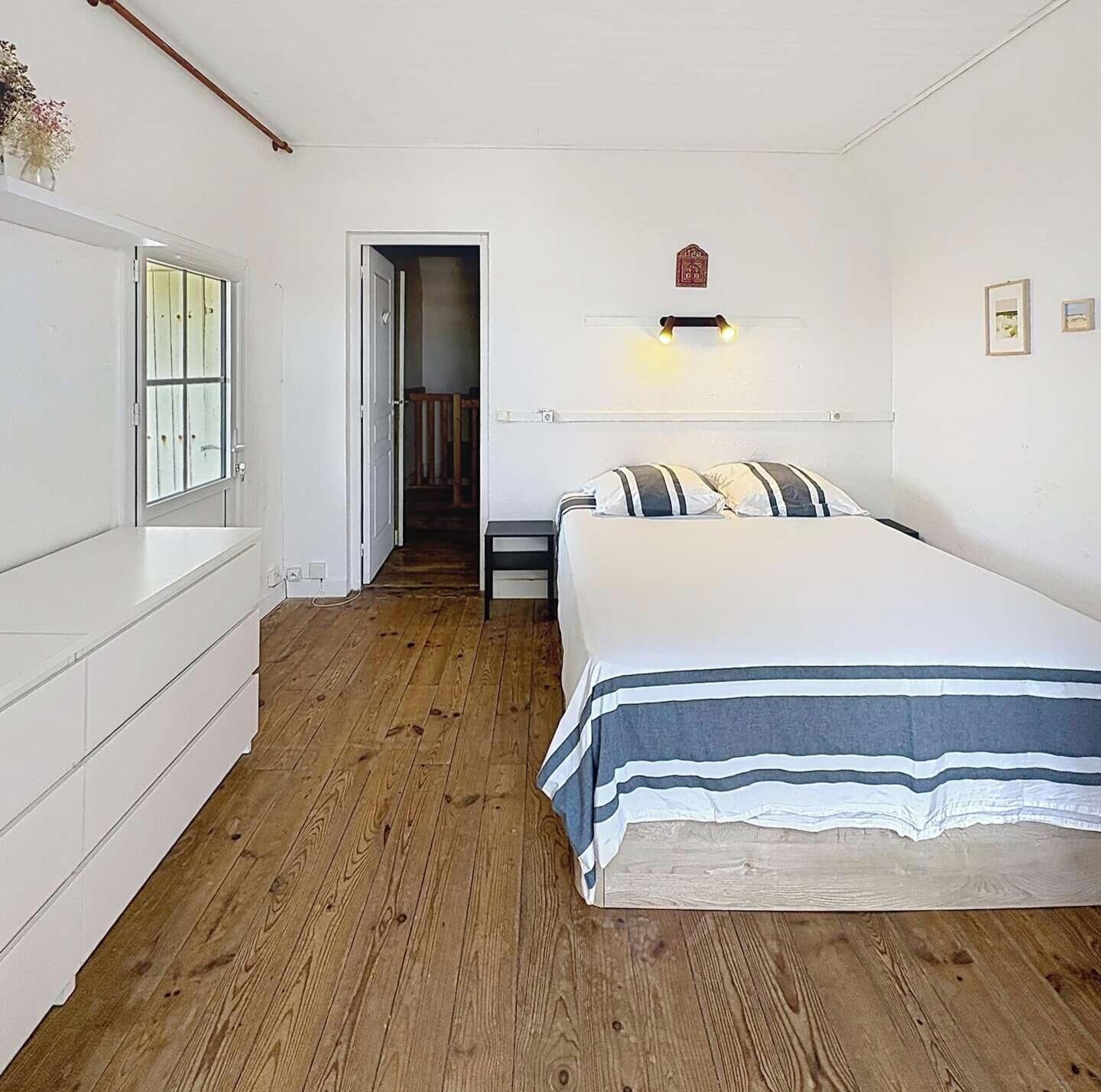 Ein Schlafzimmer mit einem Bett, einem Nachttisch, einer Kommode und einer Tür zu einem anderen Raum.