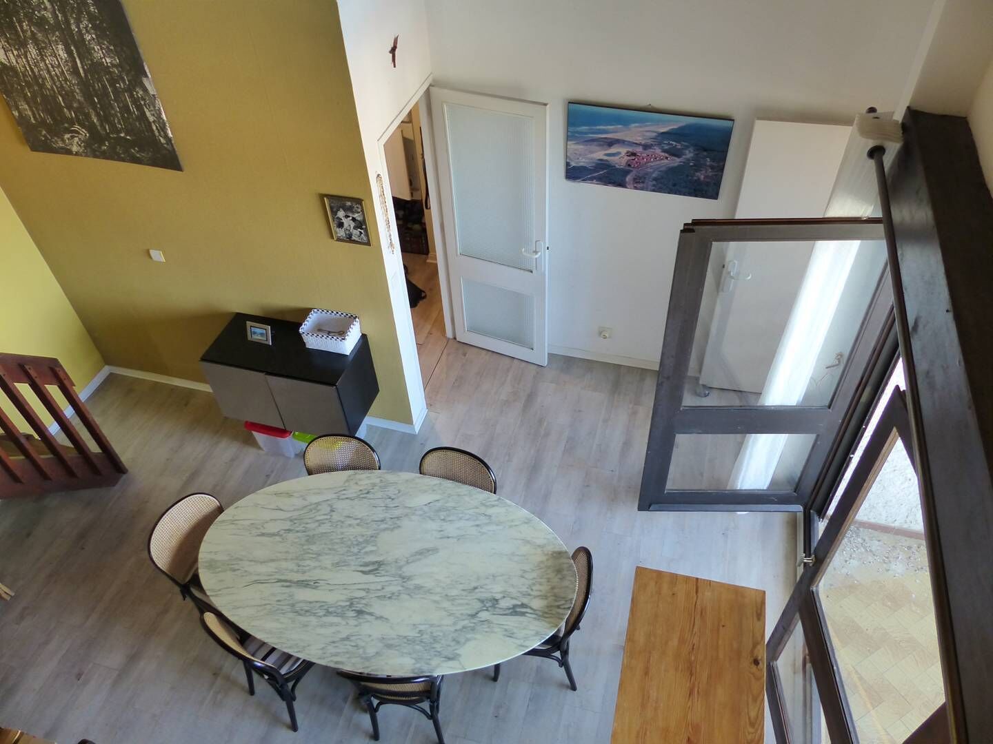 Een eetgedeelte met een marmeren tafel en stoelen, een kleine keuken met een koelkast, en een deur naar een andere kamer.
