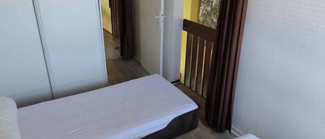 A small, narrow room with two single beds, a wooden floor, and a view of a balcony with a railing.