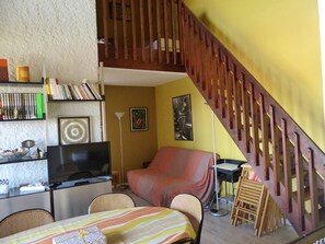 Ein Wohnzimmer mit Fernseher, Bücherregal und einer Treppe.