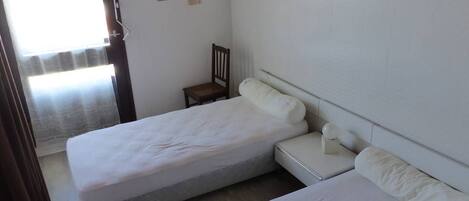 A bedroom with two beds, a chair, a framed picture on the wall, and a window with curtains.