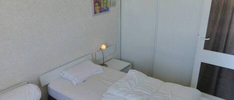 A hotel room with two beds, a bedside table with a lamp, a door with a mesh screen, and a wall with a poster.