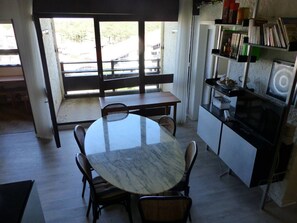 Ein Essbereich mit einem runden Tisch, Stühlen, einer Bank, einem Bücherregal und Blick durch ein Fenster.