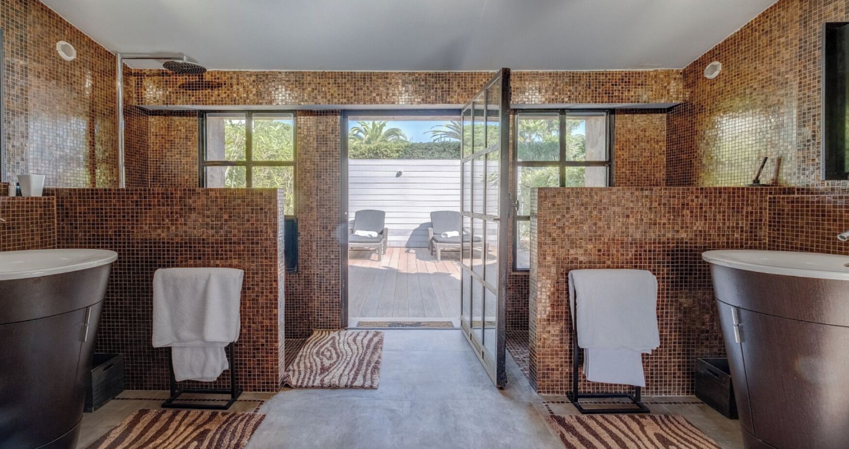 Ein Badezimmer mit zwei Waschbecken, einer Dusche und Blick auf eine Terrasse mit Gartenmöbeln.