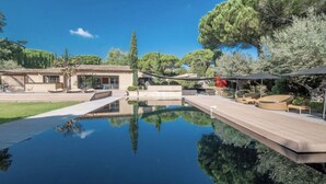 A pool with a wooden deck, outdoor seating, and a building with a tiled roof. - Villa Tahiti (Ramatuelle)