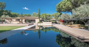 Ein Pool mit Holzterrasse, Sitzgelegenheiten im Freien und einem Gebäude mit Ziegeldach.