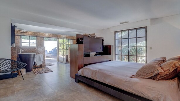 A modern bedroom with a large bed, a TV mounted on the wall, a balcony, and a seating area. - Villa Tahiti (Ramatuelle)