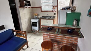 Eine kompakte Küche mit Herd, Spüle und einem grünen Kühlschrank. Zwei Holzschemeln und ein blaues Sofa sind vorhanden.