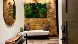 A hallway with a wooden floor, a sofa, a console table with baskets, a mirror, and a large wall-mounted artwork. - Lakeside Luxury: Hottub+Sauna+Fire Pit+Kid Friendly+Lake View+Mountain View (Whitefish)