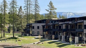 A modern multi-story building with a courtyard, surrounded by trees and a lake. - Lakeside Luxury: Hottub+Sauna+Fire Pit+Kid Friendly+Lake View+Mountain View (Whitefish)