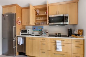 A modern kitchen with stainless steel appliances, wooden cabinets, and a microwave. - Hydrangea Lane Beach Cottage (Mashpee)