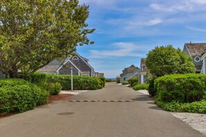 A residential street lined with houses, a clear sky, and a tree on the left. - Hydrangea Lane Beach Cottage (Mashpee)