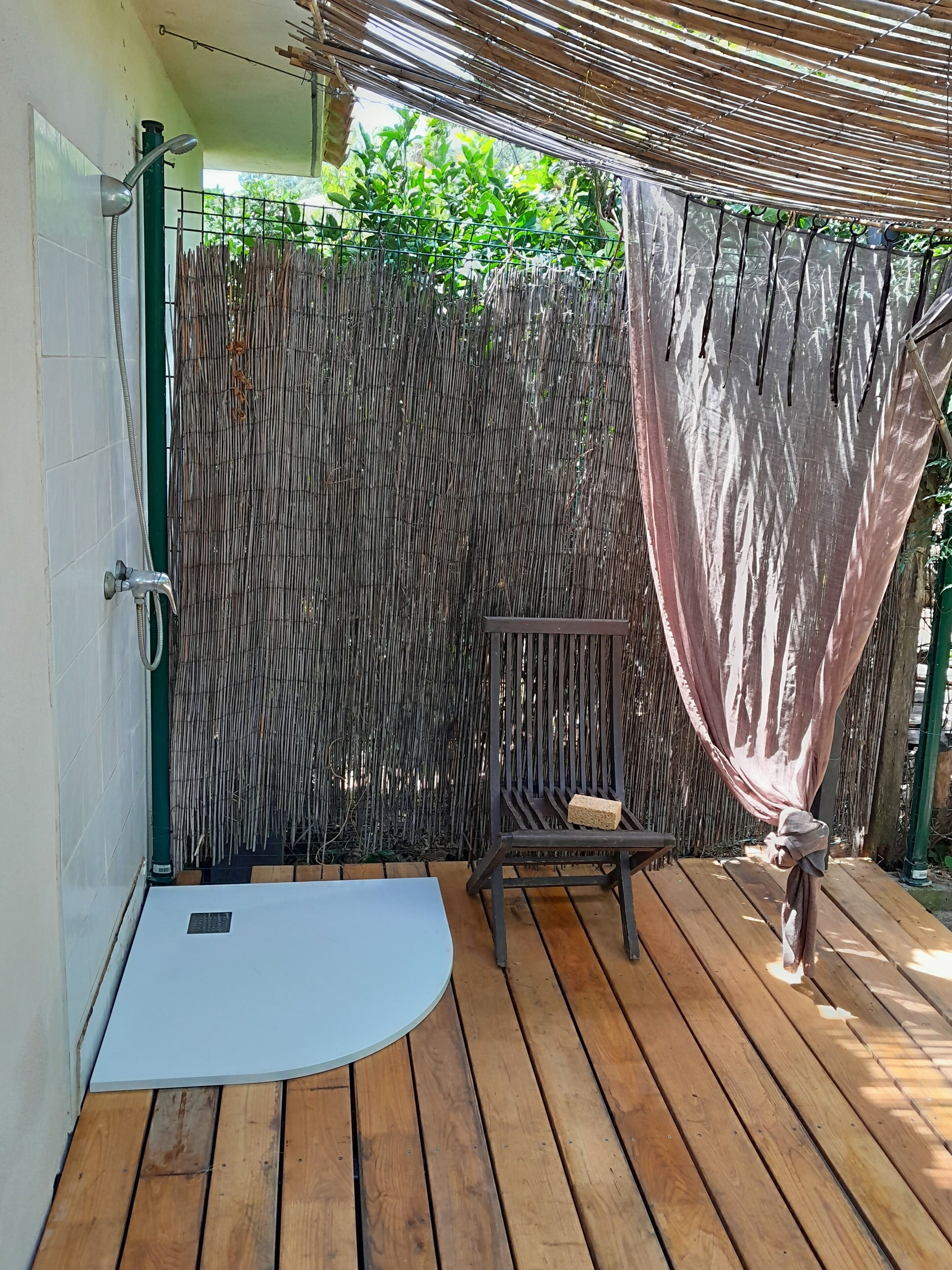 A wooden deck with a shower area, a bench, and a bamboo fence.