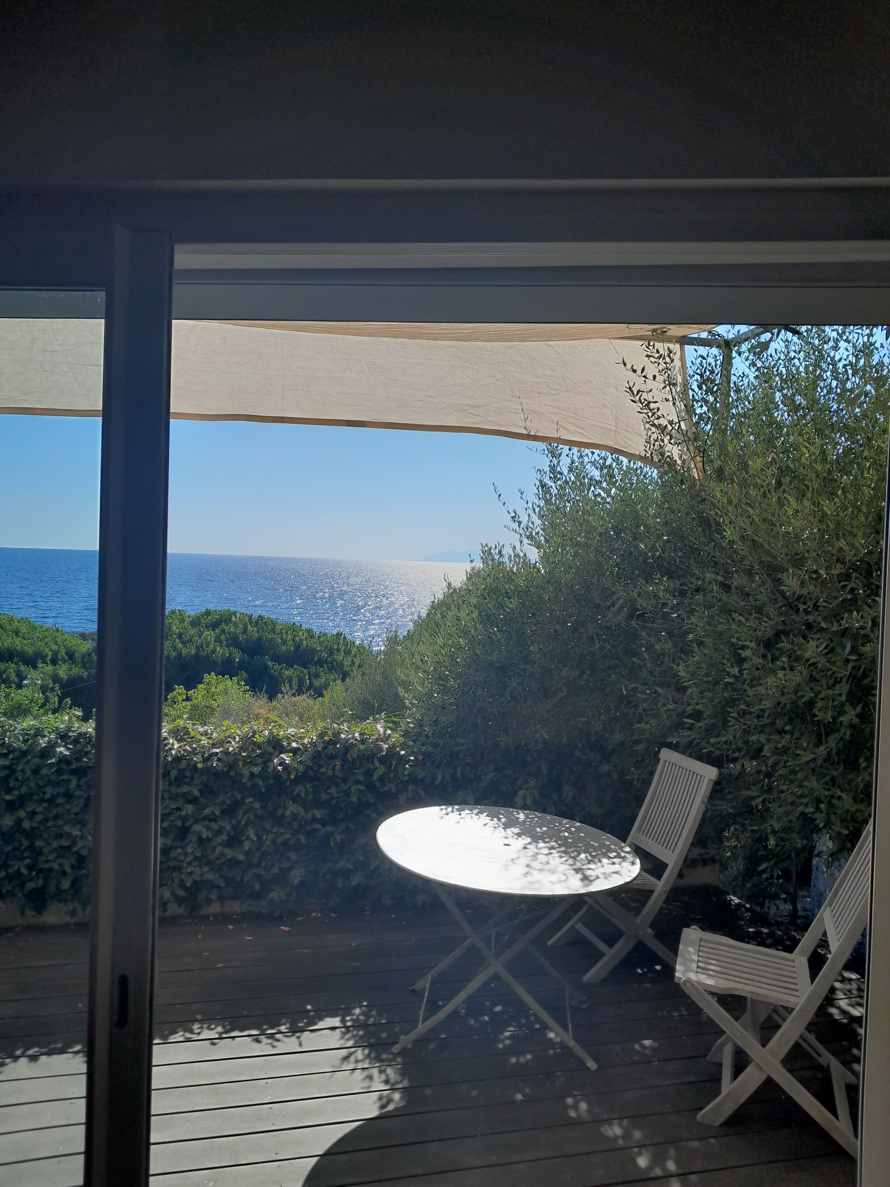 A deck with a table and chairs, overlooking a scenic view of the sea and greenery.