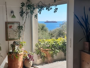 Varanda com vasos de plantas, uma obra de arte emoldurada e vista para o mar com um navio.