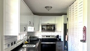 Una cocina compacta con gabinetes blancos, microondas, estufa y lavamanos.