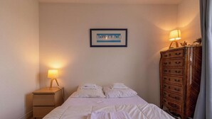 A hotel room with a bed, bedside lamps, a dresser, and a framed picture on the wall. - T3 apartment near the beach in Fréhel | 4 guests | Ref 117 (FREHEL)