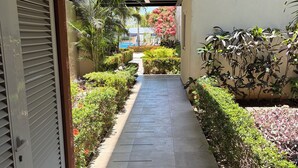 A covered walkway with a tiled floor, flanked by neatly trimmed hedges and various plants. - Comfortable apartment with a pool and hot tub. (Las Jarretaderas)