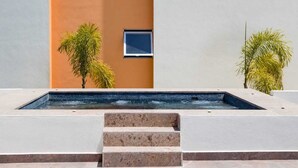 A swimming pool with steps leading up to it, surrounded by a building with a light blue and orange facade. - Comfortable apartment with a pool and hot tub. (Las Jarretaderas)
