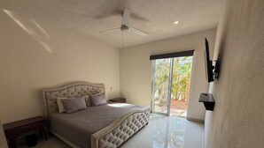 A bedroom with a large bed, a ceiling fan, a nightstand, a TV mounted on the wall, and a sliding glass door leading to a patio. - Comfortable apartment with a pool and hot tub. (Las Jarretaderas)